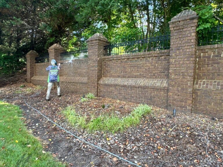 Sully's Pressure Washing technician cleaning a brick wall and fence